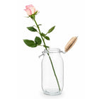 Single pink rose displayed in a glass jar with its wooden lid open, from Sharbatly.
