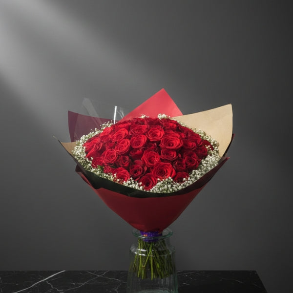 Bouquet of red roses in a clear vase on a dark surface with a gray background