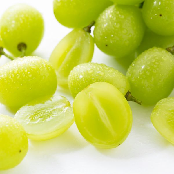 Jumbo Shine Muscat white grapes in a 1 kg bunch, fresh and plump, displayed outdoors with green leaves and sunlight.