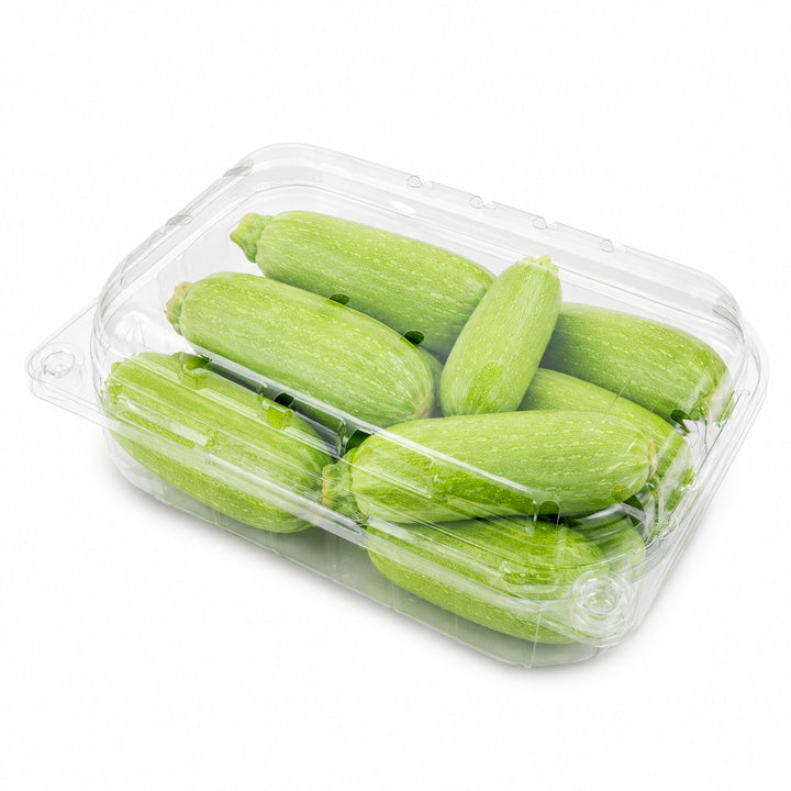 A clear plastic clamshell container holding several light green zucchini or summer squash pieces, photographed on a clean white background.