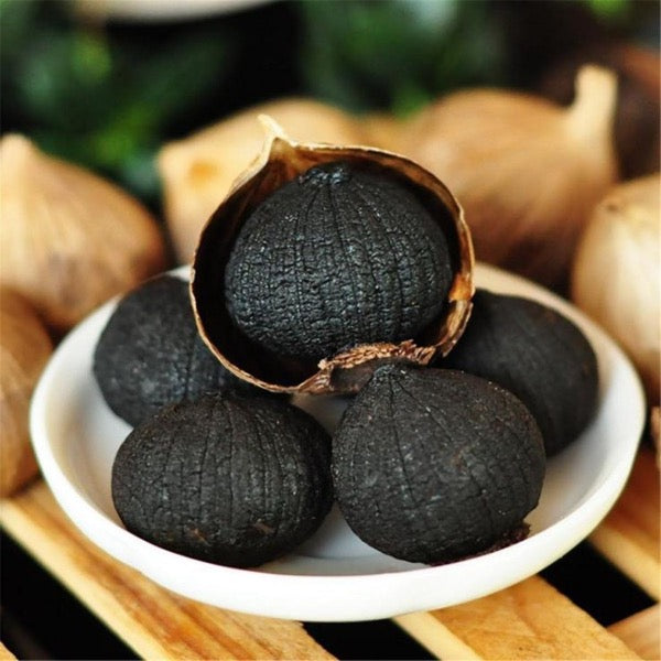 Fermented black garlic herb in a 0.25 kg pot by Sharbatly, showing dark, bulbous cloves with a smooth surface.