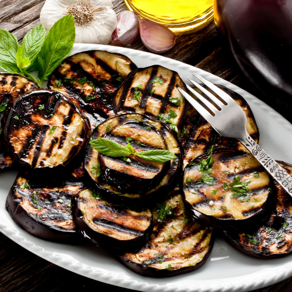 Fresh eggplants in a 1 kg bag from Local Market, showcasing glossy purple vegetable with green stems in a natural setting.